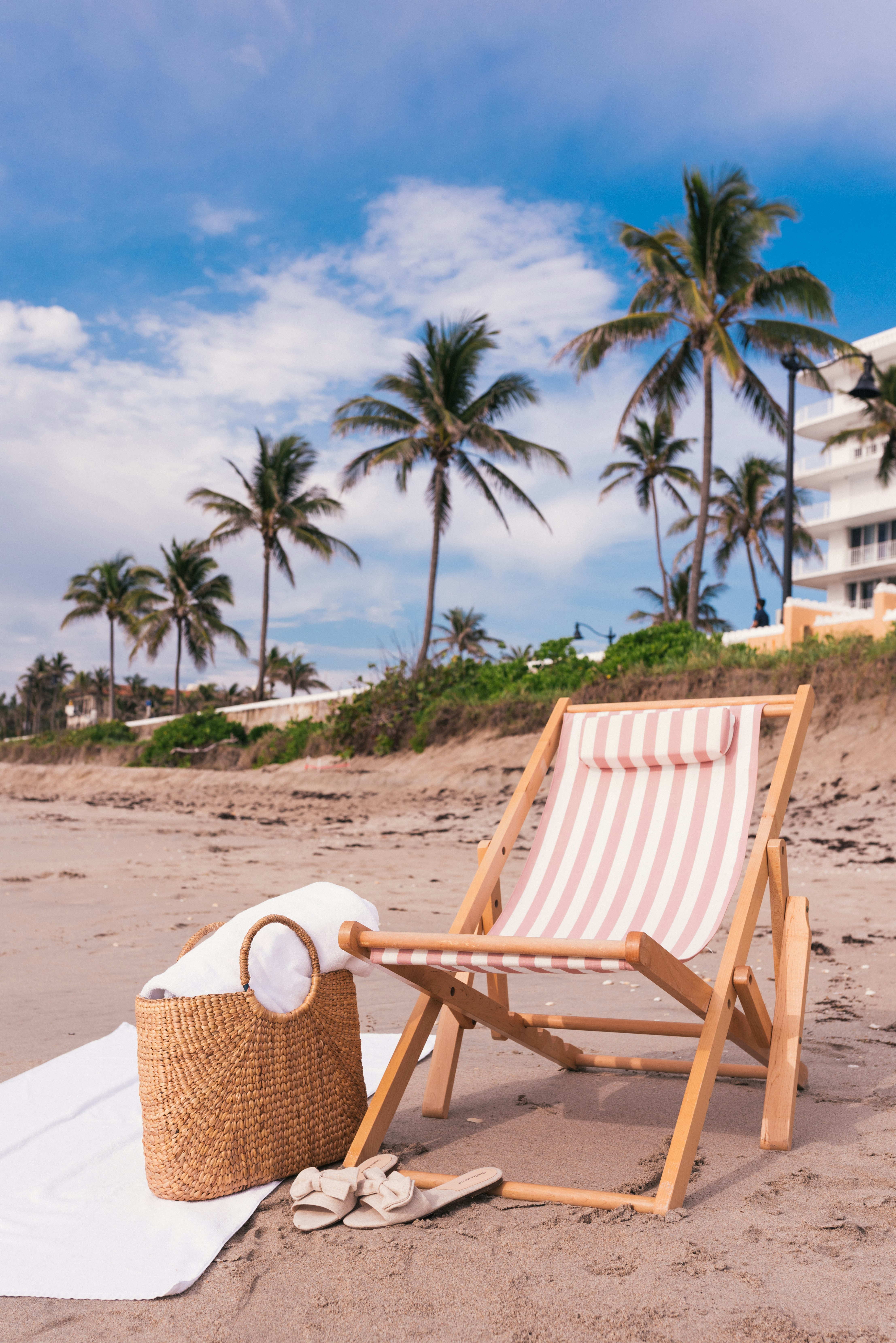 brown wicker basket near white flat sandals and beach chair on seashore under white and blue sky